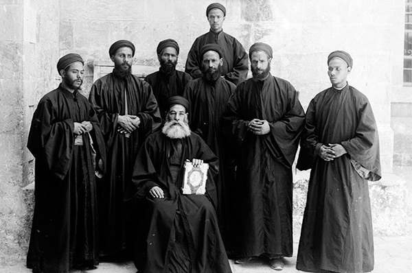 Eight Coptic clergymen in black robes, photographed outdoors in the early twentieth century